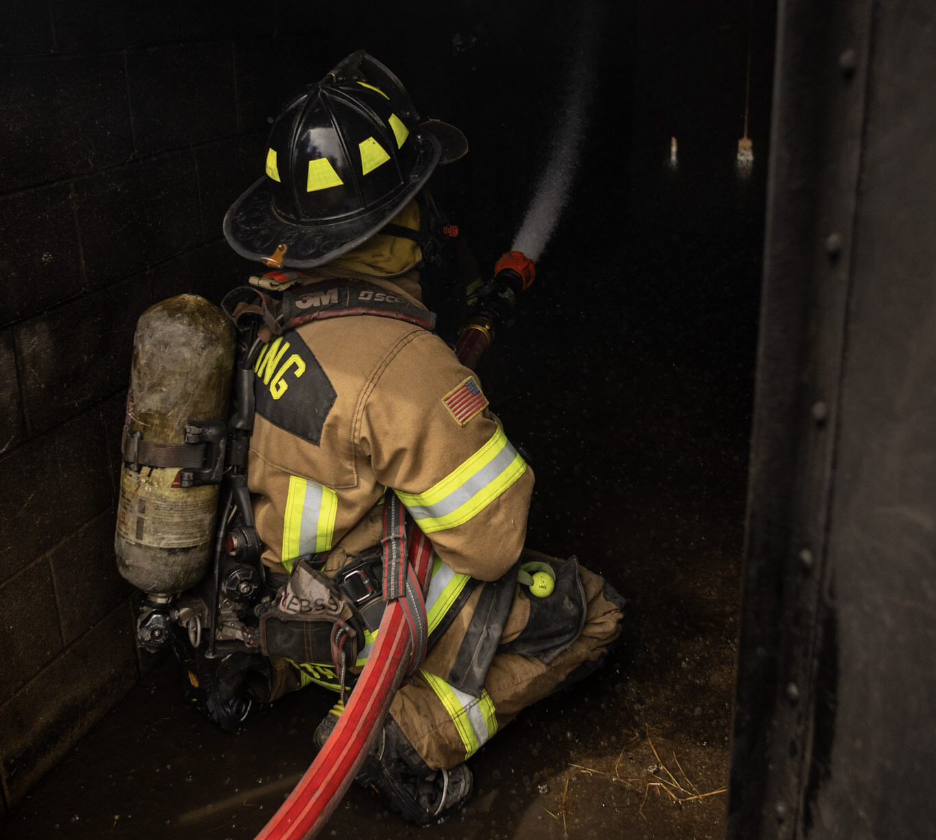 firefighter flowing water into a dark hallway