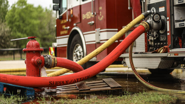 A bright red fire hose is connected between a fire hydrant and a fire truck—Mercedes Textiles Know Your Hose Resource