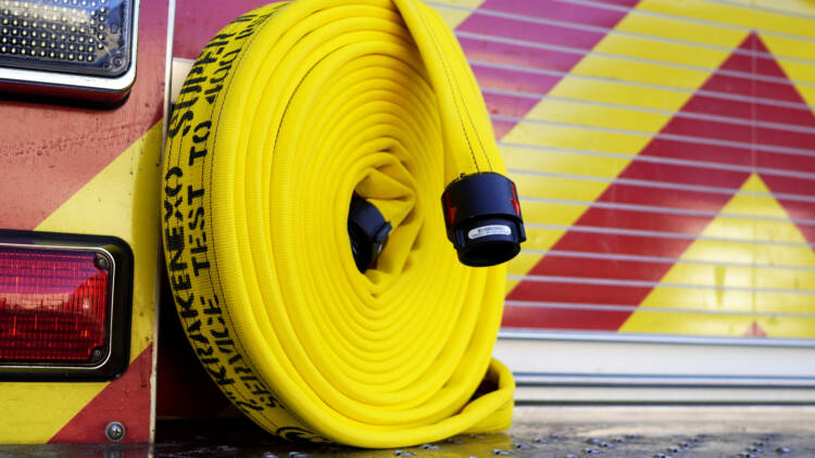 A bright yellow fire hose with the words "KrakenEXO" stamped on the side in black letters leans against a fire truck—Mercedes Textiles Know Your Hose Resource