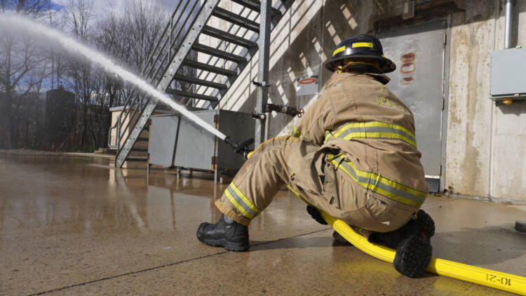 View of a fireman in his uniform facing away from the camera testing a hose—Mercedes Textiles Know Your Hose Resource